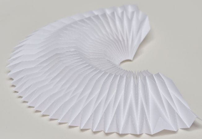 Figura semicircular de papel blanco con pliegues geométricos dispuestos en abanico, trabajo de Cartoncita