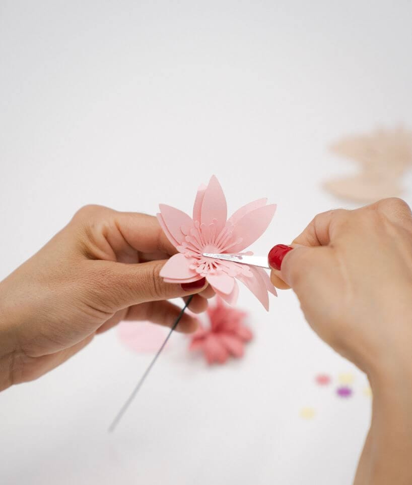 Manos sujetando una flor de papel rosa claro mientras se ajusta el centro, trabajo de Cartoncita