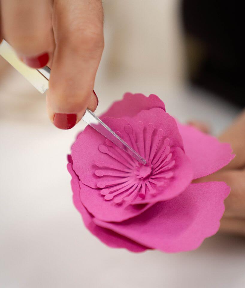 Detalle de una flor de papel rosa mientras se trabaja el centro con una herramienta manual, proceso de Cartoncita