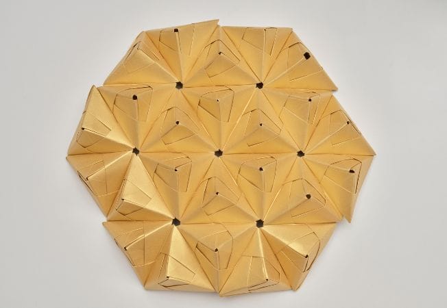 Detalle radial de módulos de papel dorado plegado formando patrón geométrico, creación de Cartoncita