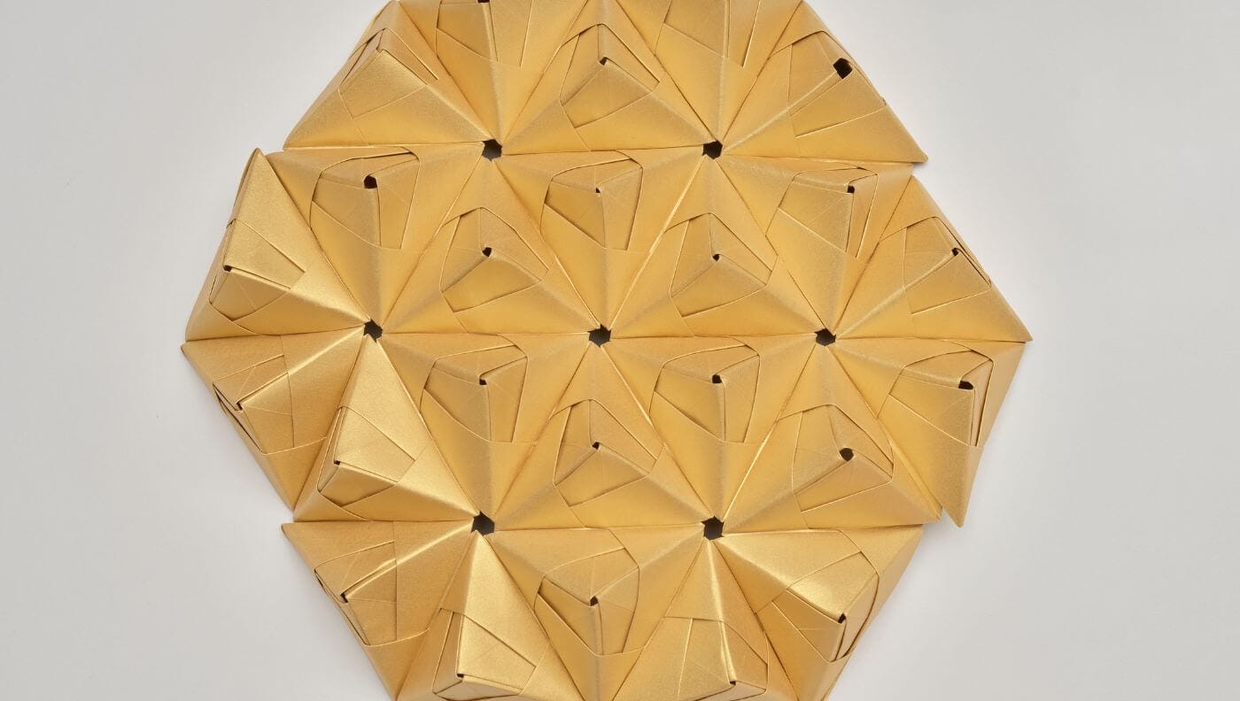 Detalle radial de módulos de papel dorado plegado formando patrón geométrico, creación de Cartoncita
